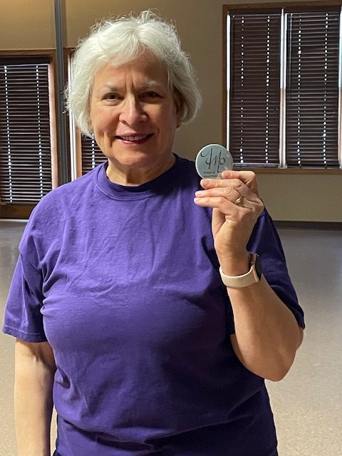 Picture of Barb Brandtner holding up the FMPL logo she designed on a button.